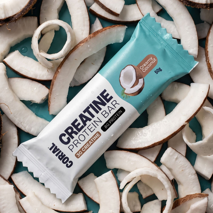 Barra proteica CORIAL com creatina Creamy Coconut sobre lascas de coco fresco
